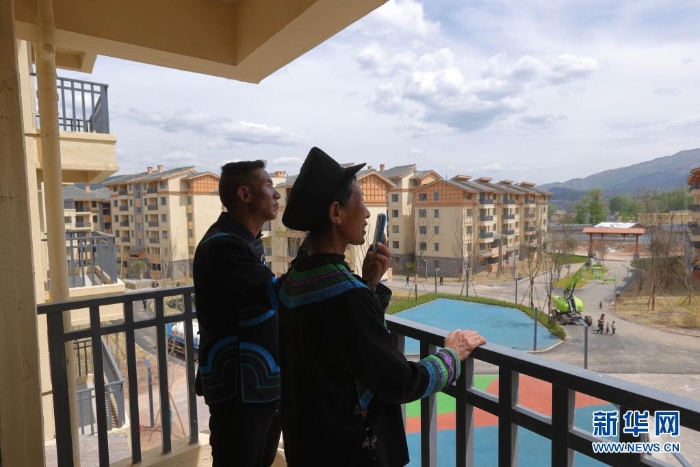在四川省昭覺縣城易地扶貧搬遷安置點南坪社區，剛搬遷到新家的“懸崖村”村民莫色達體夫婦在陽臺給親戚打電話（2020年5月13日攝）。新華社記者 江宏景 攝