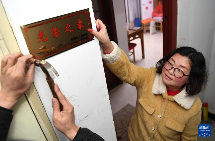 合肥市包河區(qū)常青街道工作人員在居民魏松梅（右）家門口懸掛“光榮之家”牌（2019年1月14日攝）。新華社記者 劉軍喜 攝